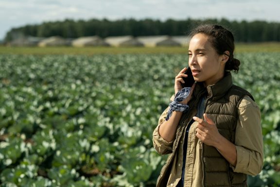 Mujer hablando por teléfono en un campo de coles, con cielo nublado al fondo.